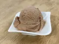 Ein Löffel cremiges Nougat Eis in einer weißen Schale auf einem Holztisch.
