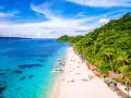 Rajska plaża na Filipinach z turkusową wodą, białym piaskiem, łodziami i zielonymi wzgórzami.