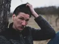 Quebonafide w czapce i swetrze, oparty o drzewo. W tle jesienny krajobraz. Tekst "żadnych zmartwień" pasuje do nastroju.