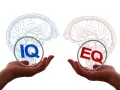 Dwie dłonie trzymają symbole IQ i EQ, symbolizujące równowagę między inteligencją a inteligencją emocjonalną.