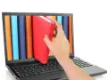 Mano saca un libro rojo de una estantería digital en una laptop. Acceso a información y al libro de IVA.