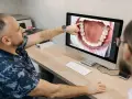 Dentysta omawia z pacjentem czyszczenie kieszonek dziąsłowych, wskazując na ekranie powiększony obraz jamy ustnej.