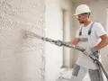 Budowlaniec nakłada tynki maszynowe. Sprawdź atrakcyjną cenę za m2 i jakość wykonania.