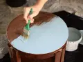 Mano aplicando pintura a la tiza color madera a una mesa redonda.
