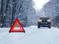 Warnblinkleuchten und Warndreieck auf verschneiter Straße. Ein Auto steht im Hintergrund. Ein wichtiger Hinweis für den auto wintercheck.