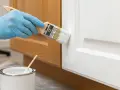 Mano con guanto blu dipinge una porta bianca con pennello. La pittura diluita è pronta per l'uso.