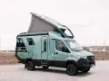 En grön Hymer Venture S husbil med uppfällt tak står parkerad vid en hamn.