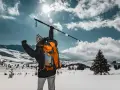 Osoba z plecakiem wznosi kijek, przygotowując się do marszu. Dowiedz się, jak prawidłowo założyć buciki na kijki nordic walking, by cieszyć się zimową wędrówką.