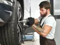 Meccanico con guanti neri lavora su una ruota. Per sapere ogni quanto girare le gomme, consulta il manuale dell'auto.