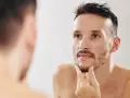 Mężczyzna zastanawia się, jak zagęścić brodę, dotykając jej palcami przed lustrem.