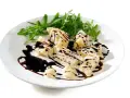 Kawałki parmezanu polane gęstą glazurą balsamiczną, podane z rukolą na białym talerzu.