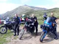 Tre motociclisti con moto da enduro posano in cima al passo San Lucio, con montagne sullo sfondo.