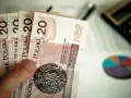 Ręka trzyma banknoty 20 zł. Obok kalkulator i wykres kołowy. Planowanie finansowe na 2025 rok, stawka godzinowa netto.