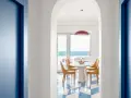 Interno di una casa stile mare con pavimento a scacchi blu e bianchi, tavolo rotondo con sedie arancioni e vista sul mare.