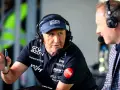Łukasz Cieślak w czapce z daszkiem i słuchawkami, gestykuluje, trzymając długopis. Obok siedzi mężczyzna w kratę.