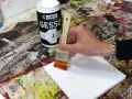 Préparation d'une toile pour faire de la peinture sur toile. Une main applique du gesso blanc avec un pinceau sur la surface vierge.