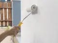 Mano aplica capa de imprimación blanca a una pared con un rodillo de pintura amarillo.