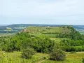 Grüne Hügel und Felder laden zum Walberla wandern ein. Ein kleiner Weg schlängelt sich zum Gipfel mit einem roten Haus.