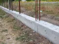 Zbrojony fundament czeka na wylewanie betonu. Widać stalowe pręty wystające z betonowej ławy fundamentowej.