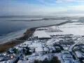 Zimowy krajobraz nad jeziorem Wicko. Lodowe tafle na wodzie, zaśnieżone pola i domy tworzą malowniczy widok.