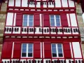 Façade rouge et blanche typique d'Espelette, avec des piments séchant. Combien de temps pour visiter Espelette ? Une journée suffit pour admirer ce village pittoresque.