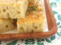Focaccia alta e soffice, tagliata a cubetti, guarnita con rosmarino e sale grosso, servita su un tagliere di legno.