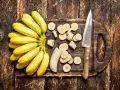 Pęczek żółtych bananów i pokrojone plasterki na desce. Dowiedz się, jak przechowywać banany, by dłużej były świeże.