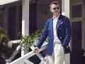 Elegancki mężczyzna w granatowej marynarce i beżowych spodniach, w stylu ivy league, stoi na werandzie.