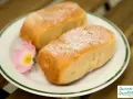 Zwei goldbraune Buchteln, bestäubt mit Puderzucker, auf einem Teller mit einer zarten rosa Blüte. Omas Rezept für Buchteln, ein Genuss!