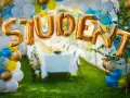 Gyllene folie ballonger bildar ordet "STUDENT" framför en festdukning utomhus.