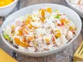 Omas Reissalat mit Orangenstücken, Schinkenwürfeln und Frühlingszwiebeln in einer Schüssel.