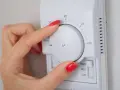 Dłoń z czerwonym lakierem reguluje termostat, ustawiając temperaturę dla elektro zaworów do CO.