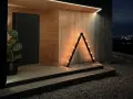 En triangulär ljusstake diy med glödlampor lyser upp entrén till ett modernt trähus.