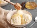 Schneeballgroße Kugeln Vanilleeis werden mit flüssigem Honig beträufelt. Ein Holzlöffel tropft goldenen Honig auf das cremige Eis.