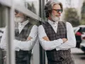Uomo con barba bianca e occhiali da sole, indossa un elegante outfit uomo gilet a quadri, camicia bianca e pantaloni scuri.