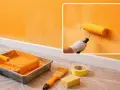 Peinture orange sur un mur, avec rouleau, bac, pinceau et ruban. La question "pourquoi mon huile mousse" pourrait être liée à la préparation de la peinture.