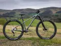 A dark grey hard tail bike with knobby tires sits on a grassy hill, ready for adventure.