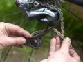 Smutsiga händer arbetar med att byta kedja på en cykel. Detaljbild på bakväxeln och kedjan.