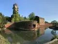 Antica torre e mura di mattoni circondate da un fossato, un angolo suggestivo di Venezia e dintorni, con vegetazione rigogliosa.