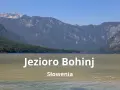 Spokojne jezioro Bohinj w Słowenii otoczone zielonymi wzgórzami i skalistymi górami.