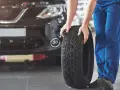 Mechanik pokazuje, jak założyć opony w dobrym kierunku. Widać bieżnik i czarne auto.