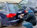 Mężczyzna montuje tablicę rejestracyjną na samochodzie Audi A4. Nowa rrs rejestracja gotowa do drogi.