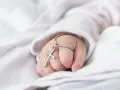 Dziecięca dłoń z krzyżykiem na srebrnym łańcuszku na białym tle.