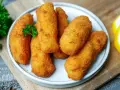 Knusprige kroketten aus kartoffelbrei, goldbraun frittiert, garniert mit Petersilie und Zitronenspalten.