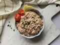 Un bol de rillettes de thon, garni de tomates cerises et de quartiers de citron, prêt à être dégusté.