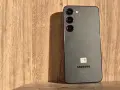 Szary Samsung S23 z trzema obiektywami aparatu na drewnianym tle. Długo działająca bateria pozwoli Ci cieszyć się nim przez cały dzień.