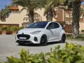 Biała Mazda 2 Hybrid zaparkowana przed budynkiem z palmami. Stylowy miejski samochód gotowy na podróż.