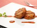 Dos manitas de cerdo rebozadas y fritas, servidas con salsa roja y perejil en un plato blanco.