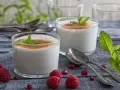 Zwei Gläser cremiger Leche Merengada, garniert mit Minze und Zimt, umgeben von Himbeeren und Granatapfelkernen.
