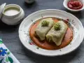 Dwa gołąbki w sosie pomidorowym, udekorowane kiełkami. Pytanie brzmi: czy gołąbki można mrozić? Obok sos śmietanowy i ketchup.